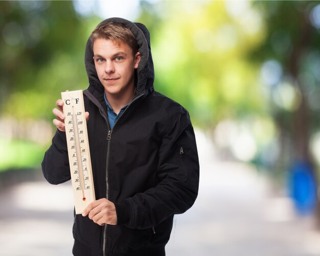 Mann mit Sweatshirt mit einem großen Thermometer