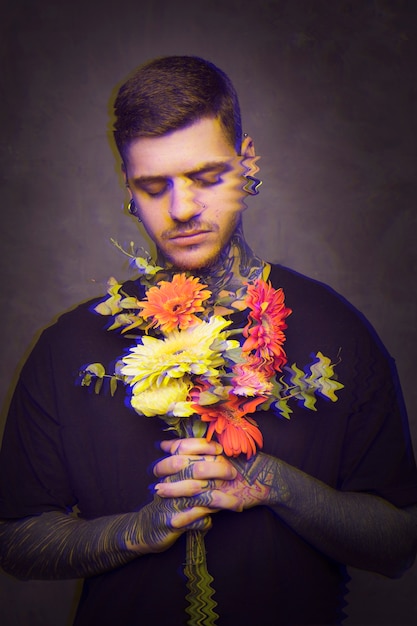 Mann mit Tätowierungen, die einen Blumenstrauß von Blumen halten