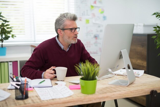 Mann mit Tasse Kaffee, der am Computer arbeitet