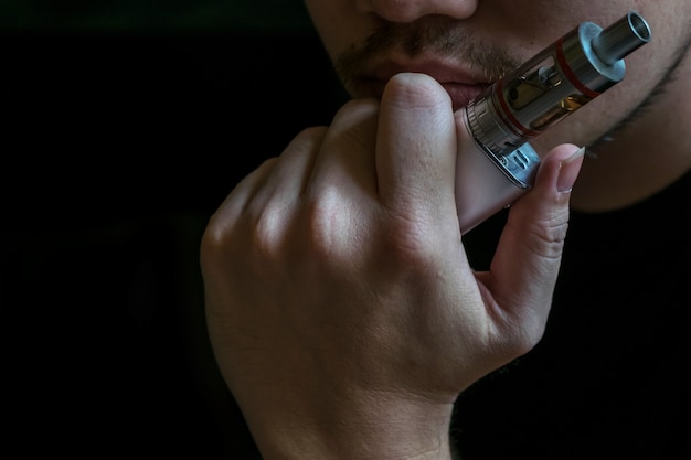 Mann mit verdeckter Identität Rauchen eine umstrittene Vaping eine elektronische Zigarette. Vaping ist in der Gesundheitsgemeinschaft umstritten, wenn es sicher ist oder ein Gesundheitsrisiko ist