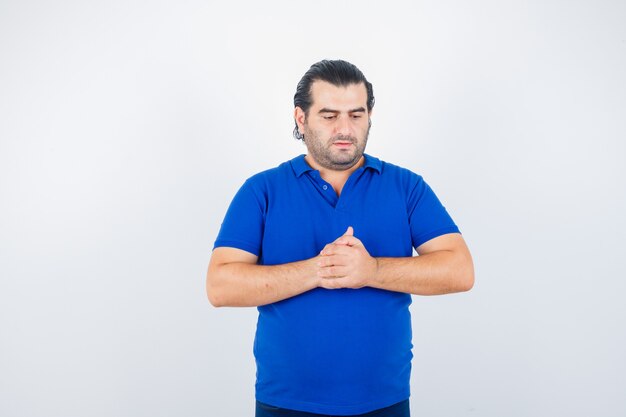 Mann mittleren Alters, der gefaltete Hände im Polo-T-Shirt zeigt und verärgert aussieht