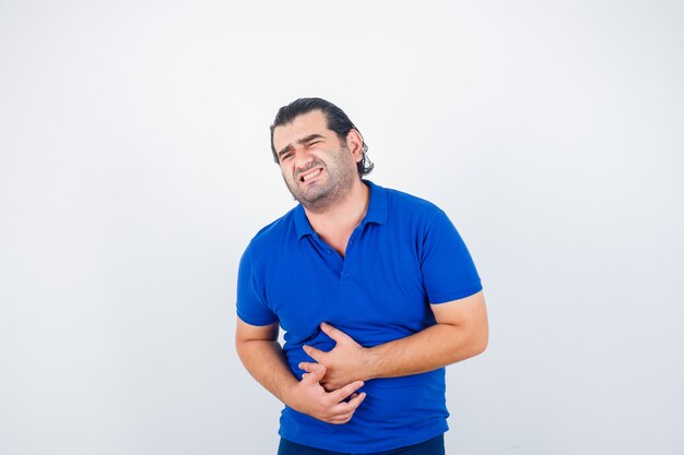 Mann mittleren Alters im blauen T-Shirt mit Magenschmerzen