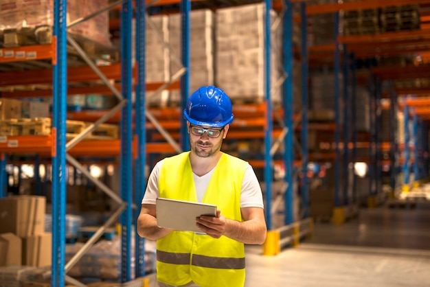 Mann mittleren Alters in schützender Arbeitskleidung, die an einer Tablette im großen Lagerlager arbeitet