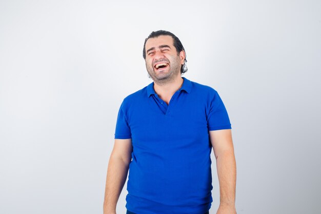 Mann mittleren Alters lacht im blauen T-Shirt und schaut fröhlich, Vorderansicht.