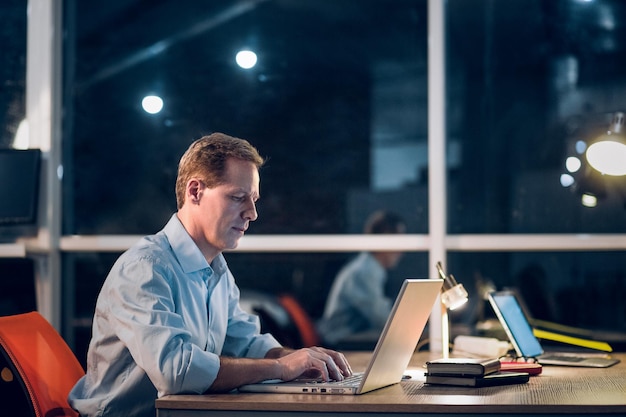 Mann mittleren Alters sitzt am Tisch und arbeitet mit Laptop