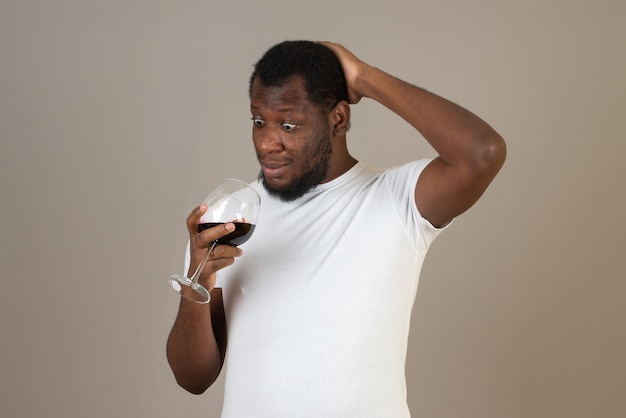 Mann schaut auf ein Glas Wein in der Hand und steht vor der grauen Wand