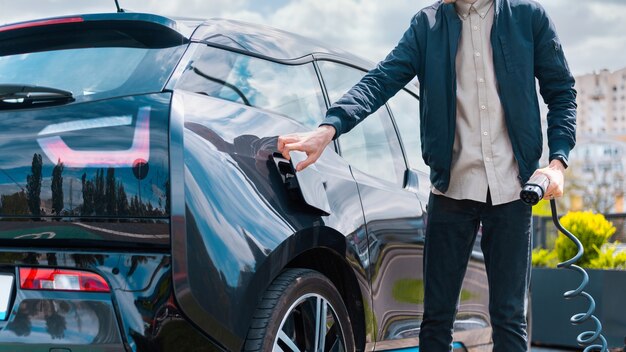 Mann schließt die Ladebuchse des Autos und hält das Ladegerät an der Ladestation