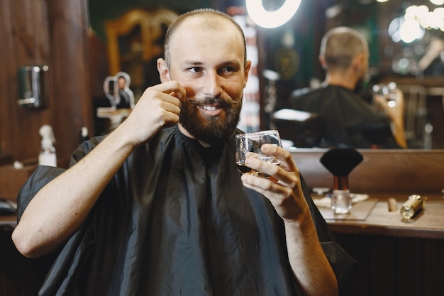 Mann sitzt auf einem Stuhl. Friseur mit einem Kunden. Guy trinkt einen Whisky.