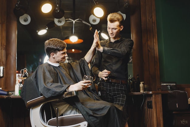 Mann sitzt auf einem Stuhl. Friseur mit einem Kunden. Guy trinkt einen Whisky.