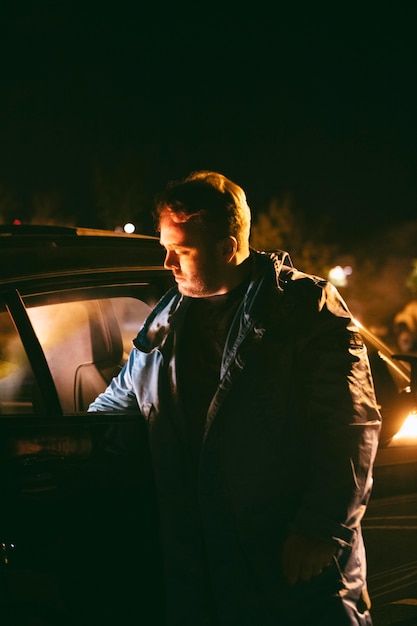 Kostenloses Foto mann sitzt nachts neben dem auto