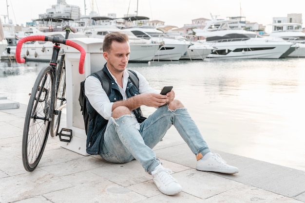 Mann sitzt neben seinem Fahrrad und spielt am Telefon