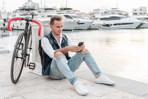 Mann sitzt neben seinem Fahrrad und spielt am Telefon