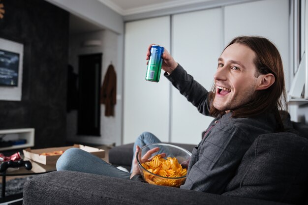 Mann sitzt zu Hause drinnen und isst Chips fernsehen