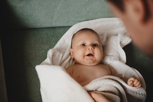 Mann spielt mit einem kleinen neugeborenen Baby, das in weiche Decke eingehüllt wird