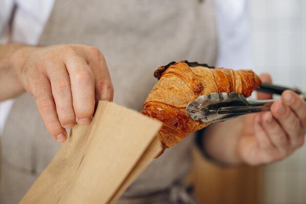 Mann steckt Croissant mit einer Zange in eine Papiertüte