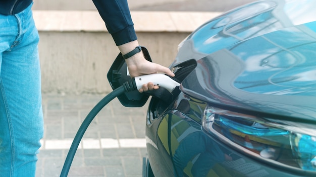 Mann steckt das Ladegerät an der Ladestation in ein Elektroauto ein