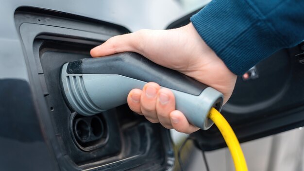 Mann steckt das Ladegerät an der Ladestation in ein Elektroauto ein