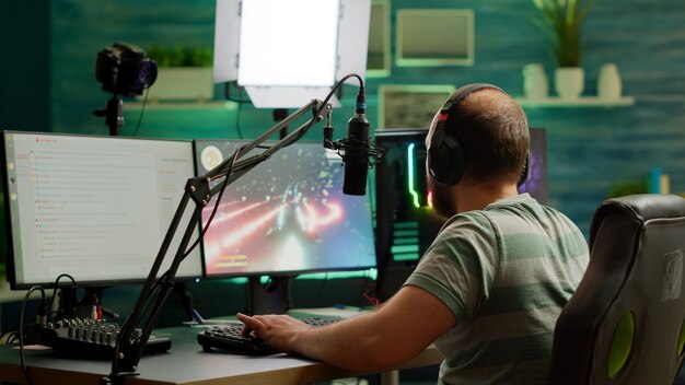 Mann-Streamer, der ein Space-Shooter-Videospiel mit Headset spielt, über Stream-Chat und Mikrofon spricht. Online-Streaming von Cyber-Performances auf einem professionellen RGB-Computer während eines Gaming-Turniers