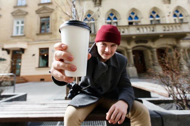 Mann streckt seine Hand mit der Tasse Kaffee aus, die auf der Bank sitzt