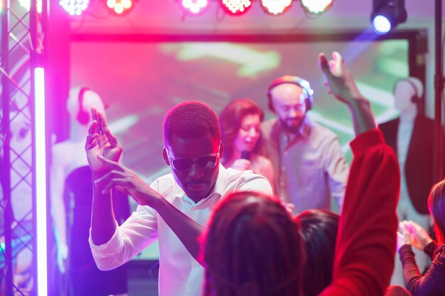Mann tanzt mit Freunden und feiert in der Diskothek im Nachtclub. Junger afroamerikanischer Clubber hat Spaß und macht Bewegungen auf der Tanzfläche bei einem Konzert mit elektronischer Musik im Club