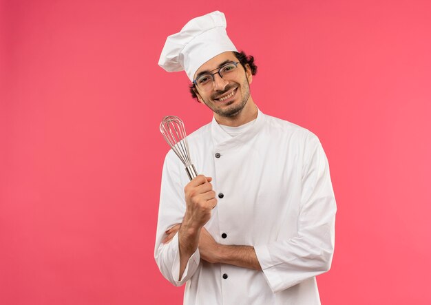 Mann trägt Kochuniform und Brille, die Schneebesen lokalisiert auf Rosa hält