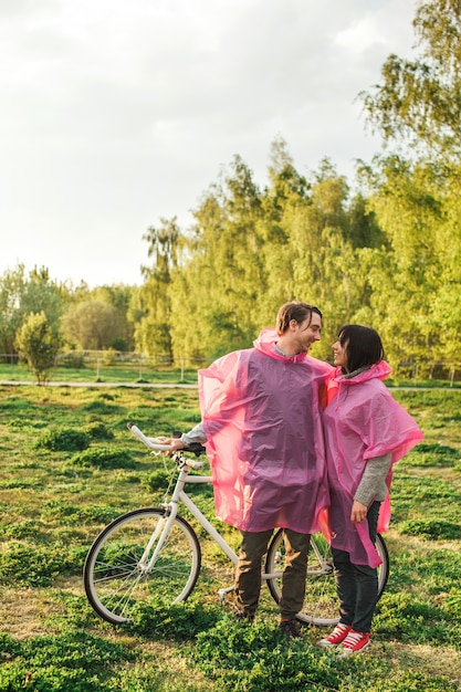 Mann und eine Frau, die romantisch jeweils in rosa Plastikregenmänteln an einem Datum mit einem Fahrrad betrachten