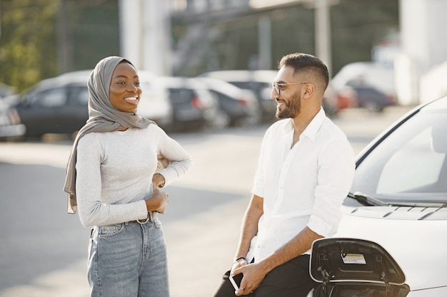 Mann und Frau des jungen Paares, die zusammen reisen. Machen Sie Halt an der Autoladestation.