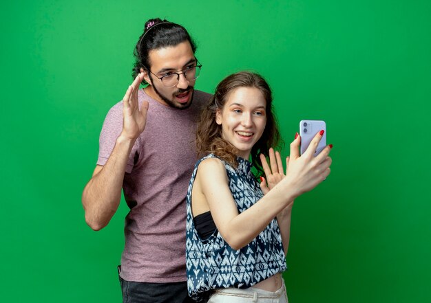 Mann und Frau des jungen Paares, glückliche Frau, die Foto von ihnen unter Verwendung ihres Smartphones macht, das über grünem Hintergrund steht