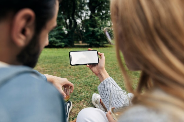 Mann und Frau, die ein Telefon beim Picknick im Freien betrachten