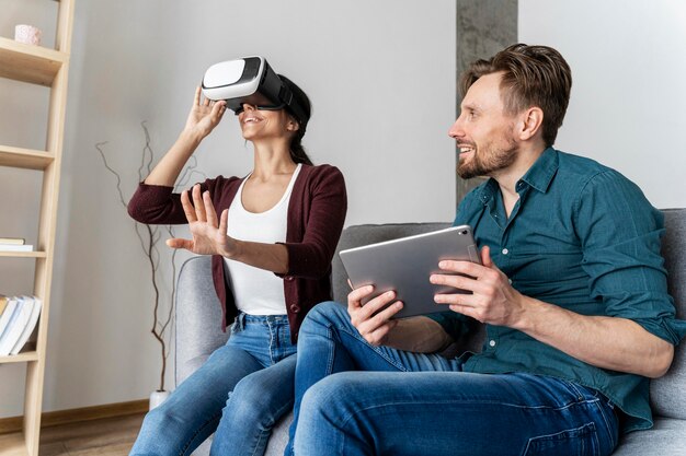 Mann und Frau haben Spaß zu Hause beim Spielen mit Virtual-Reality-Headset und Tablet