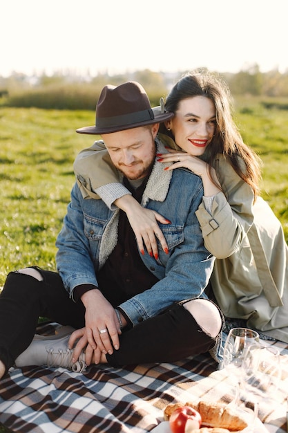 Mann und Frau in modischer Kleidung sitzen auf einer Natur auf einer Picknickdecke. Mann mit Jacke und schwarzem Hut und Frauenmantel