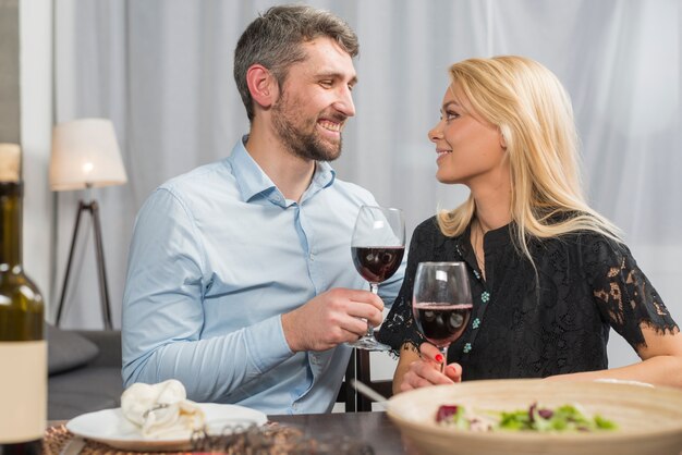 Mann und Frau mit Gläsern des Getränks bei Tisch mit Schüssel Salat