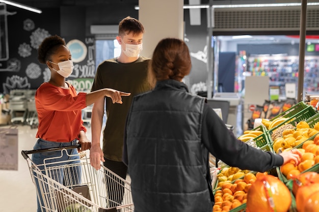 Mann und Frau mit medizinischen Masken beim Lebensmitteleinkauf mit Einkaufswagen