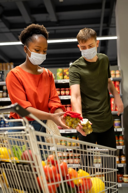 Kostenloses Foto mann und frau mit medizinischen masken beim lebensmitteleinkauf mit einkaufswagen