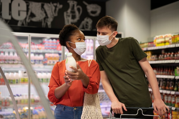 Mann und Frau mit medizinischen Masken beim Lebensmitteleinkauf mit Einkaufswagen
