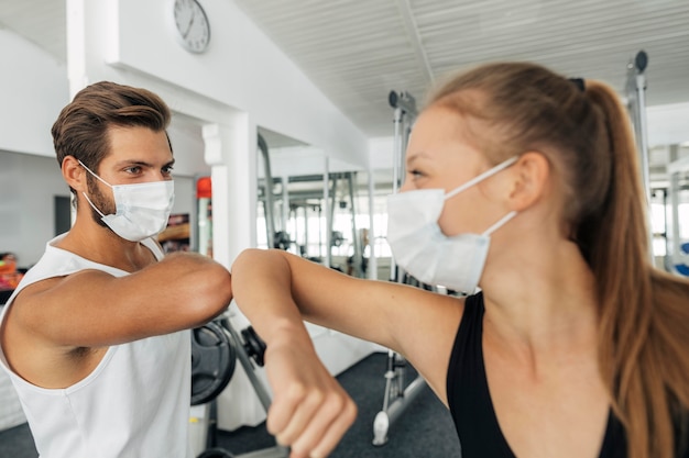 Mann und Frau mit medizinischen Masken, die den Ellbogengruß im Fitnessstudio tun