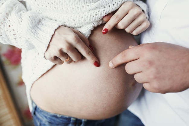 Mann und Frau mit roten Nägeln berühren mit ihren Fingern ihren schwangeren Bauch