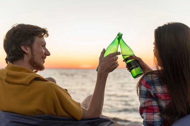 Kostenloses Foto mann und frau rösten mit bierflaschen bei sonnenuntergang