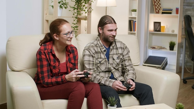 Mann und Frau sitzen auf dem Sofa und spielen Videospiele mit drahtlosem Controller.