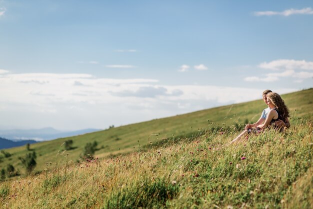 Mann und Frau sitzen, umarmend auf dem Gras vor schöner Landschaft