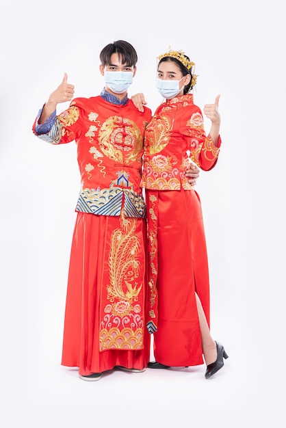 Mann und Frau tragen Cheongsam-Anzug und Maske. Die Daumen bis zur Veranstaltung werden am chinesischen Neujahrstag stattfinden