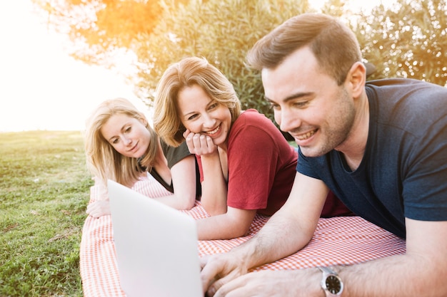 Mann und Frauen, die Laptop auf Picknick durchstöbern