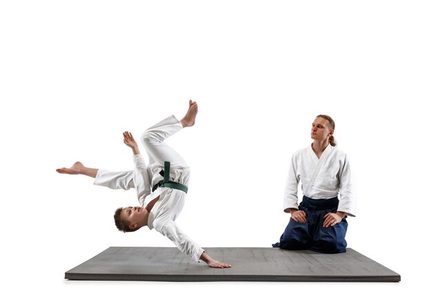 Mann und jugendlicher Junge kämpfen am Aikido-Training in der Kampfkunstschule. Gesunder Lebensstil und Sportkonzept. Kämpfer im weißen Kimono auf weißer Wand. Karate-Männer mit konzentrierten Gesichtern in Uniform.