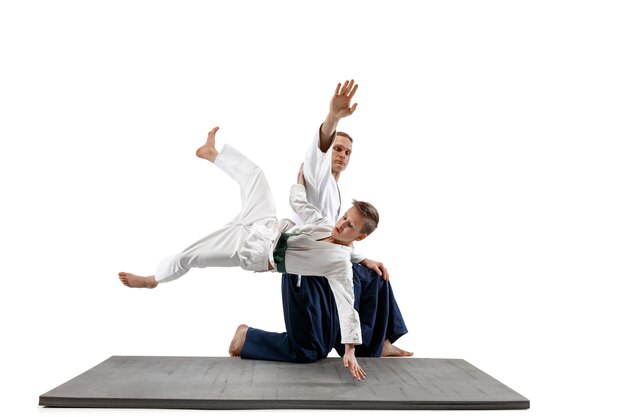 Mann und jugendlicher Junge kämpfen am Aikido-Training in der Kampfkunstschule. Gesunder Lebensstil und Sportkonzept. Kämpfer im weißen Kimono auf weißer Wand. Karate-Männer mit konzentrierten Gesichtern in Uniform.