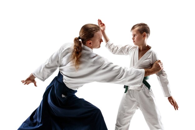 Mann und jugendlicher Junge kämpfen am Aikido-Training in der Kampfkunstschule. Gesunder Lebensstil und Sportkonzept. Kämpfer im weißen Kimono auf weißer Wand. Karate-Männer mit konzentrierten Gesichtern in Uniform.