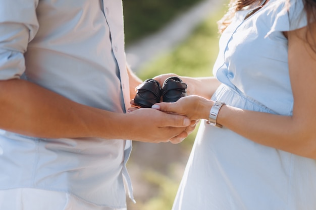 Mann und schwangere Frau halten Schuhe für neugeborenes Baby in ihren Armen, die auf dem grünen Feld stehen