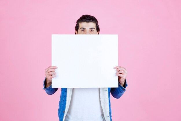 Mann versteckt sein Gesicht hinter einer quadratischen Denktafel