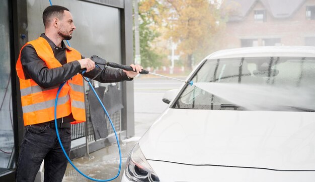 Mann wäscht Auto auf Autowaschanlage mit orangefarbener Weste