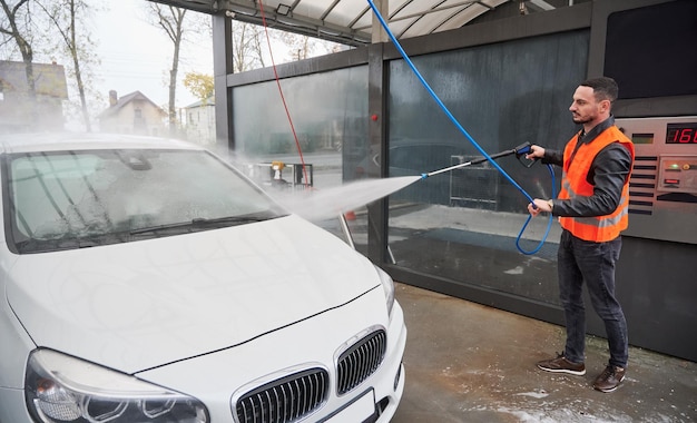 Kostenloses Foto mann wäscht auto auf autowaschanlage mit orangefarbener weste