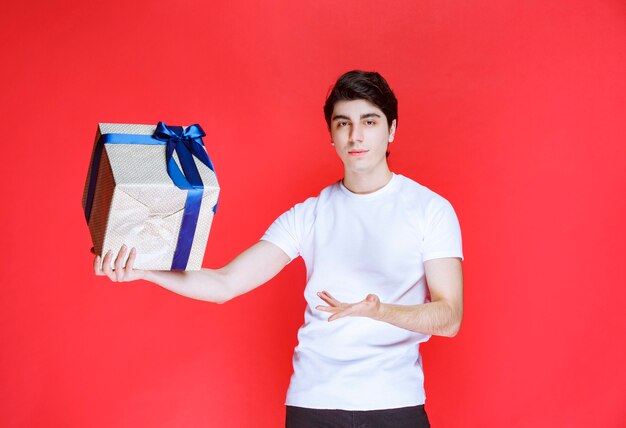 Mann zeigt auf seine weiße Geschenkbox mit blauem Band